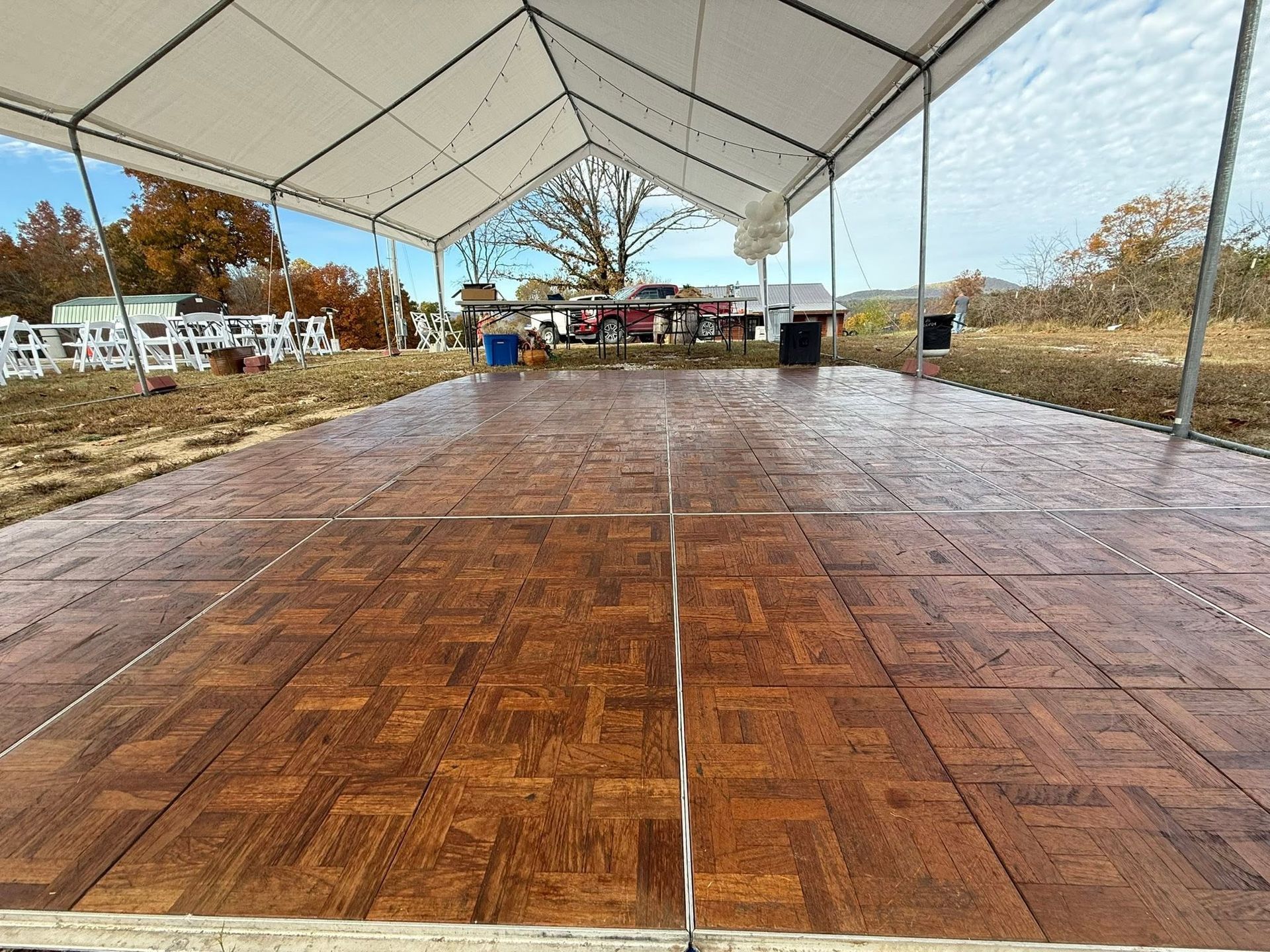 Empty wooden dance floor under a white canopy outdoors, with trees and fencing in the background