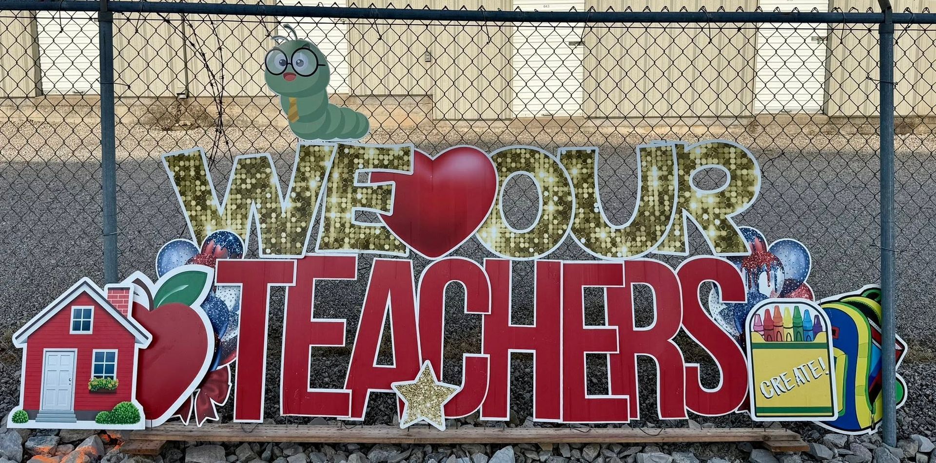 Colorful “We Heart Our Teachers” sign with a red schoolhouse and decorative school-themed graphics