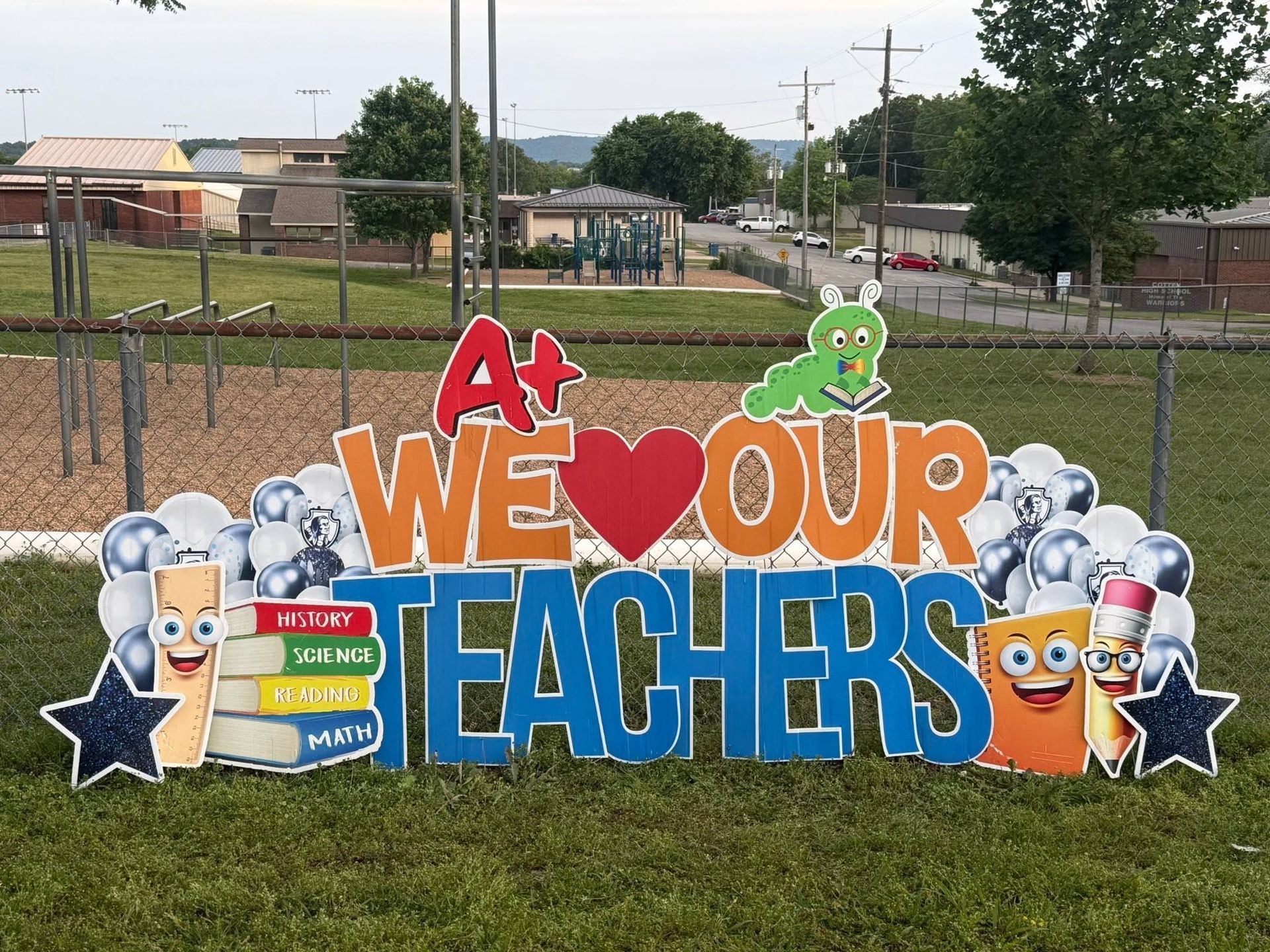 Colorful “We Love Our Teachers” schoolyard sign with stars and cartoon school supplies.