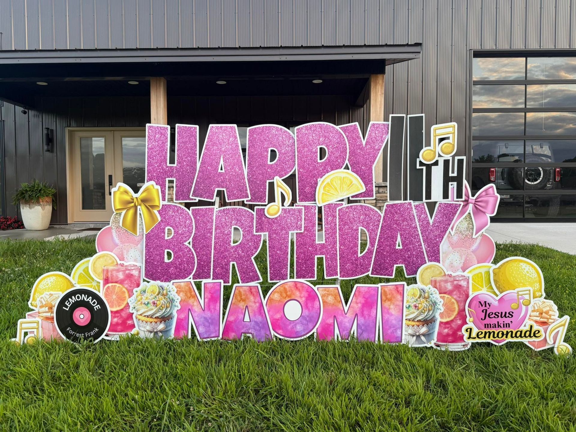 Pink “Happy Birthday Naomi” balloon display in front of a building with floral and bee decorations