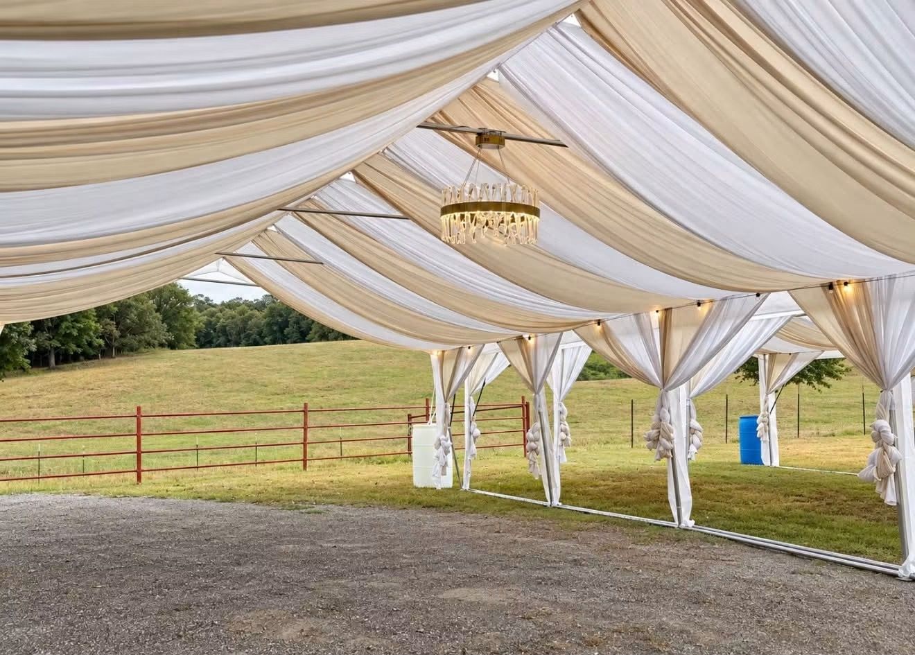 White draped canopy tent over gravel at an outdoor event venue with grassy field beyond