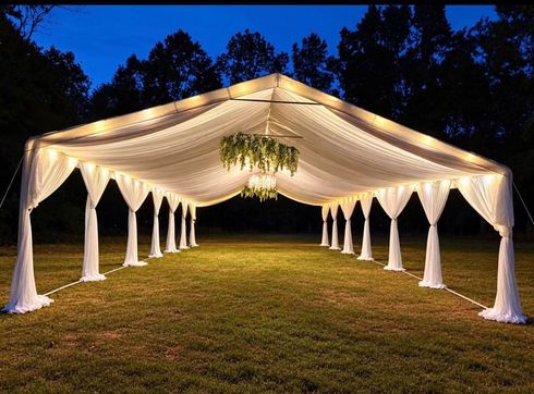 White draped wedding tent lit at dusk on a grassy lawn, with hanging greenery centerpiece