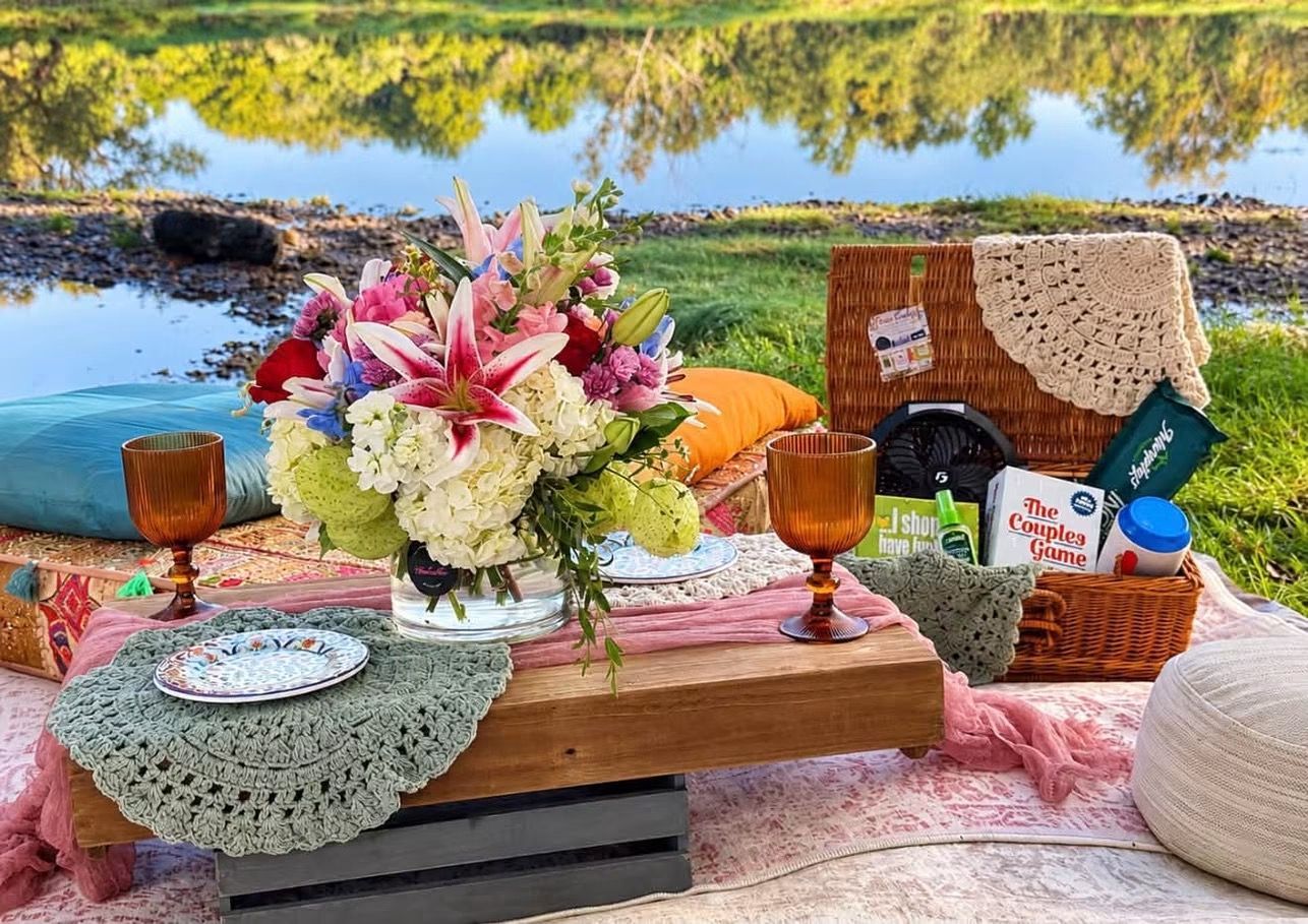 Picnic setup with flowers, snacks, and drinks on a blanket by a lakeside in autumn