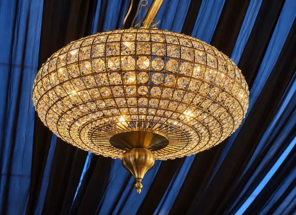 Ornate crystal chandelier glowing against blue draped ceiling panels