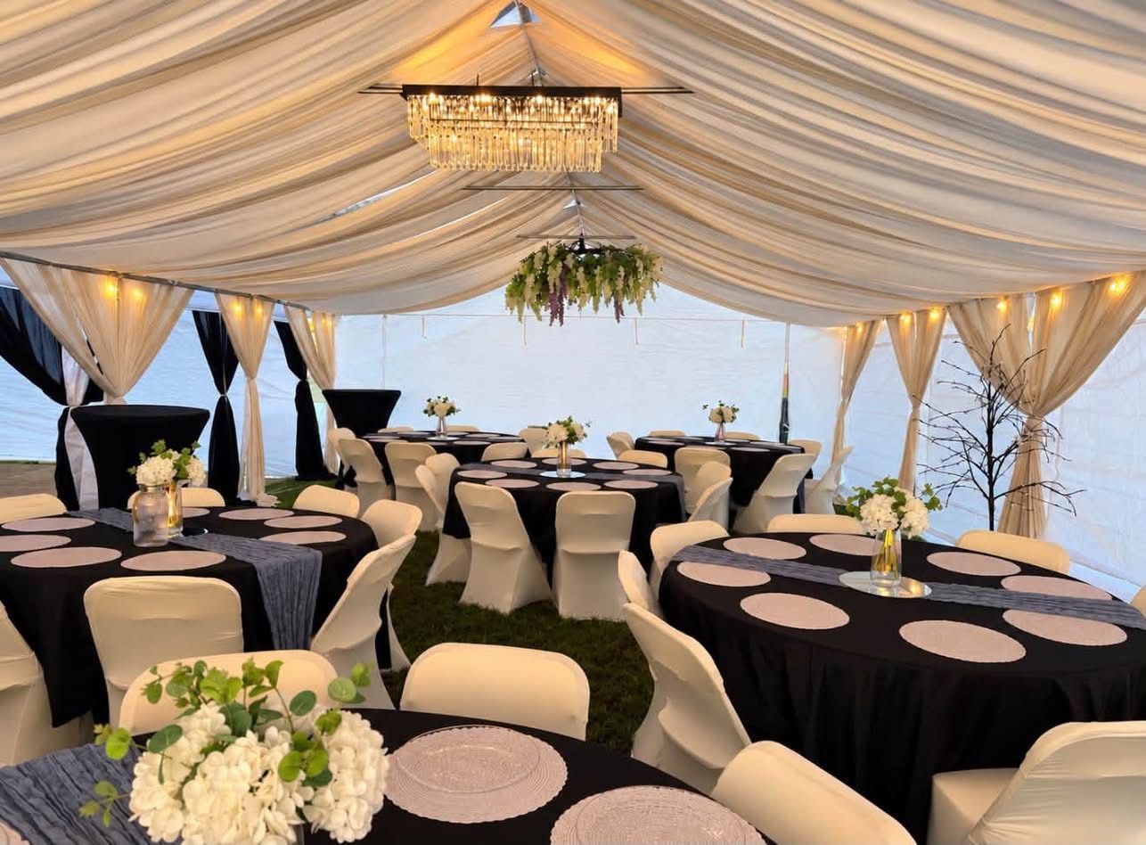 Elegant tented event space with black-and-white table settings, white drapes, and hanging floral decor