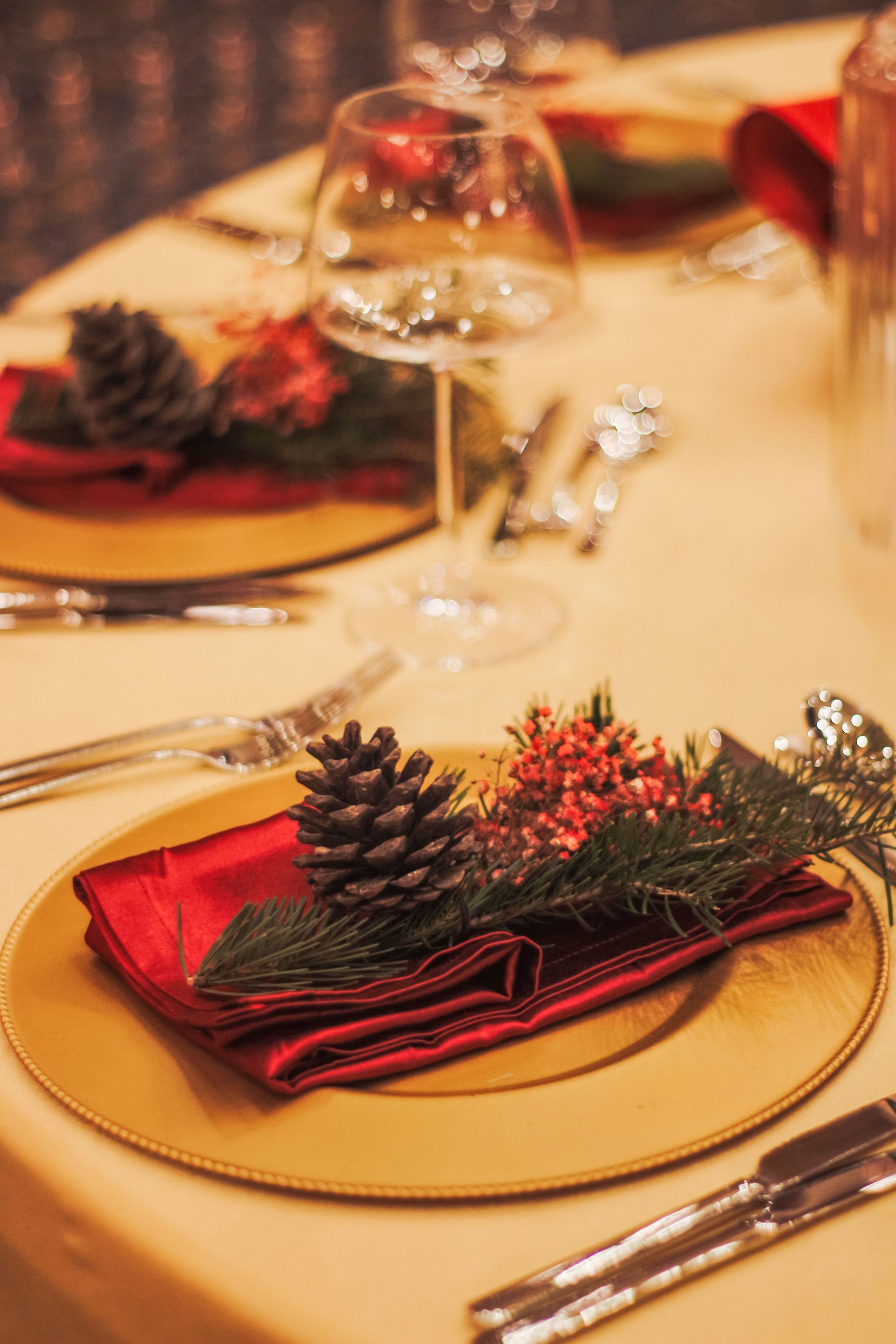 Festive table setting with red napkins, pinecones, and gold plates in warm candlelight
