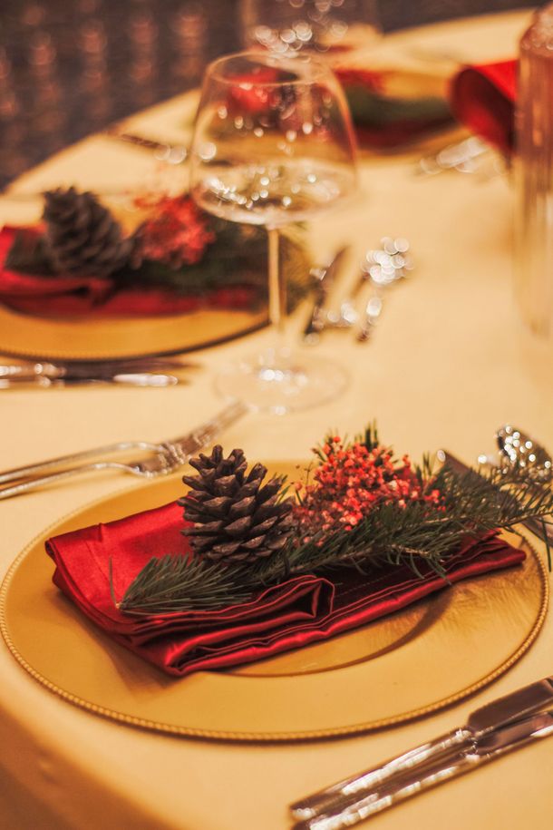 Festive table setting with red napkins, pinecones, and gold chargers on a warmly lit dining table