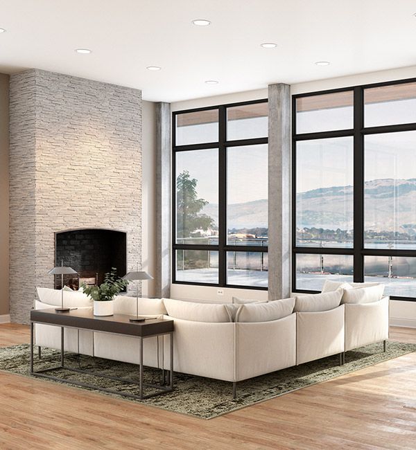 Modern living room with beige sectional, fireplace, wood floor, and large windows overlooking water and mountains
