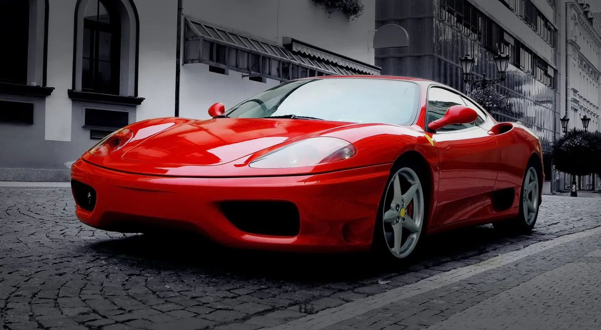 Red Ferrari sports car parked on a cobblestone street with buildings in the background.