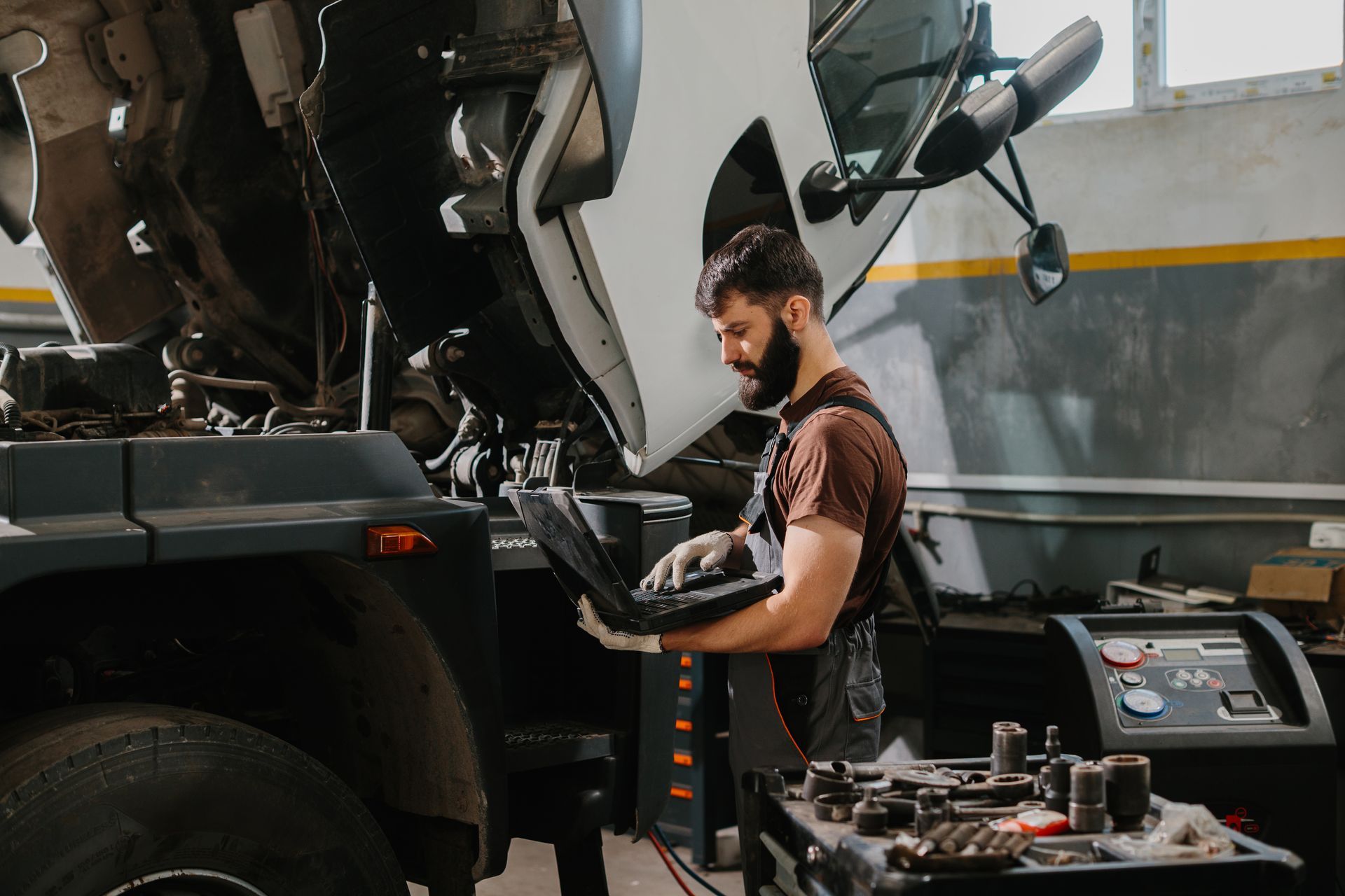 Mechanic using a laptop to diagnose a vehicle's engine in a garage.
