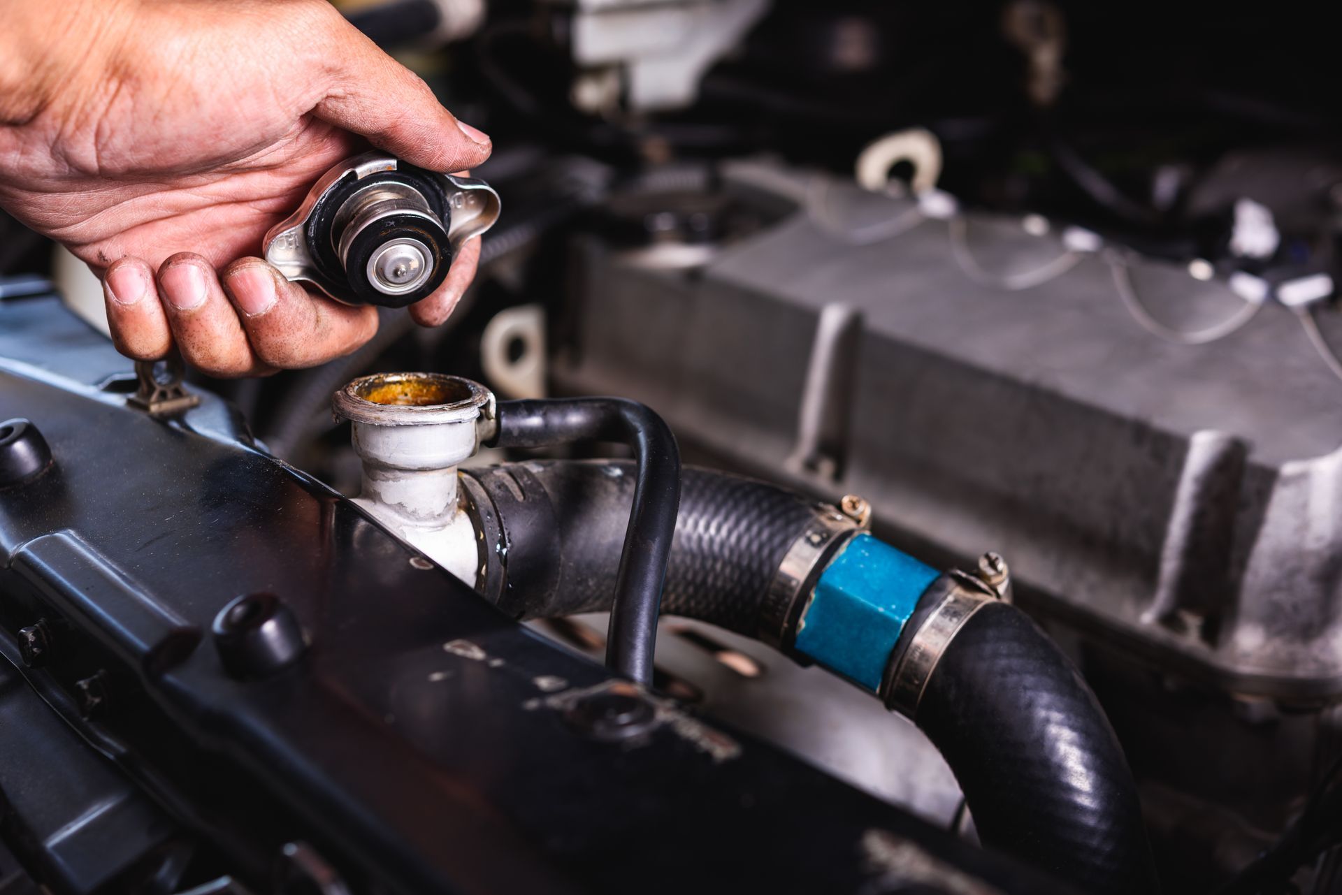 Hand opening a radiator cap on a car engine, revealing the radiator.