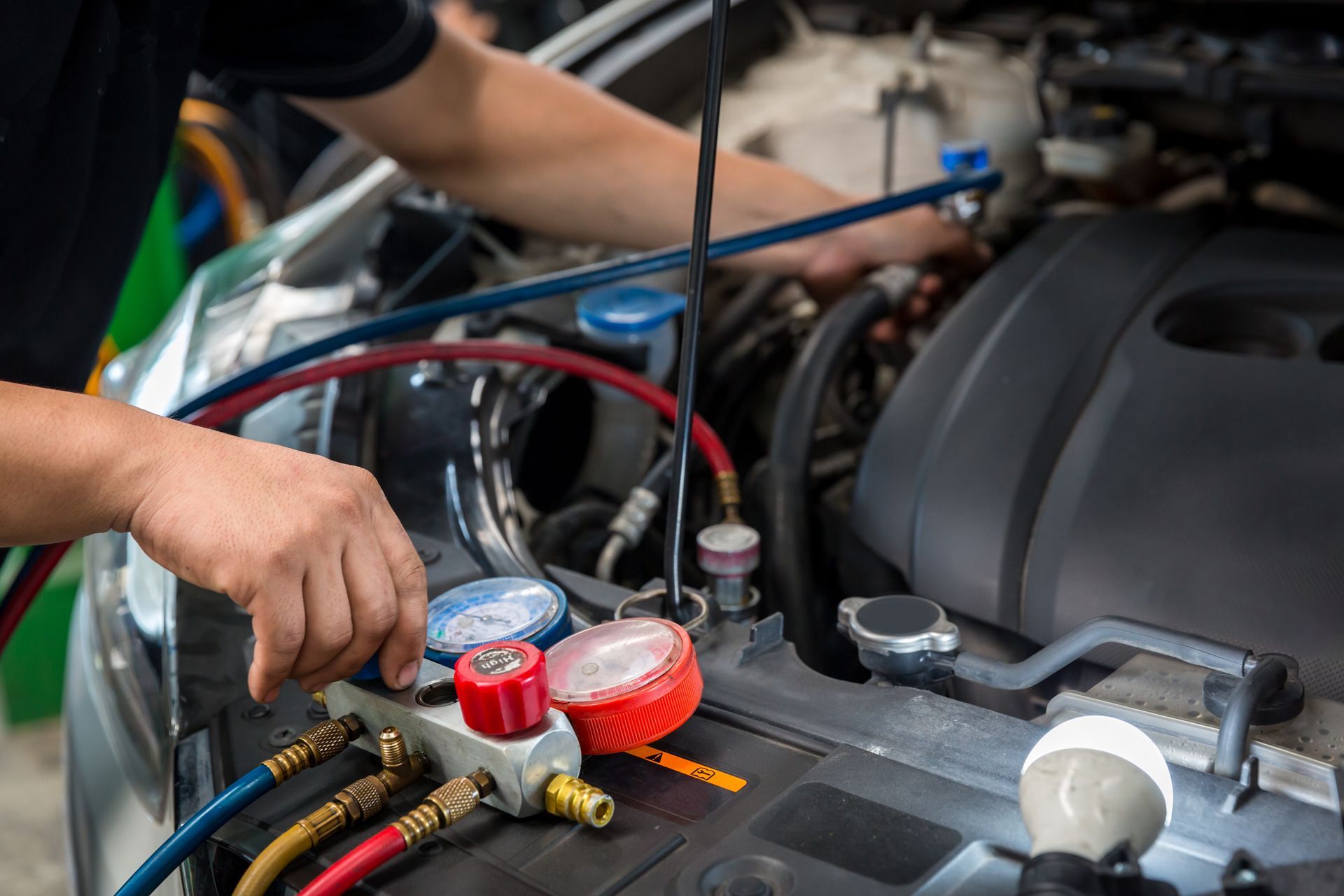 Mechanic working on car engine, attaching gauges and hoses for AC service.