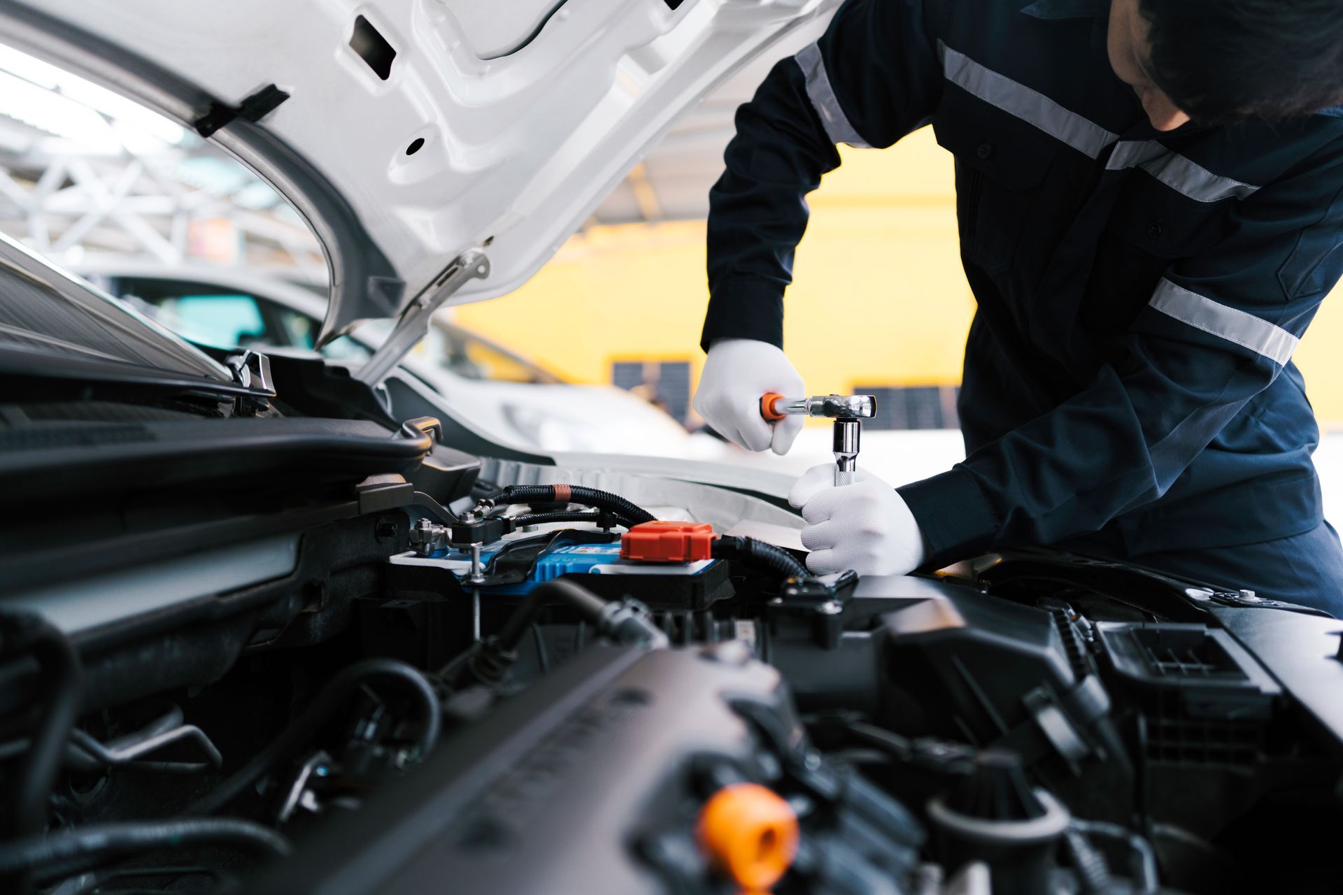 Mechanic working on car engine, using wrench. Hood open.