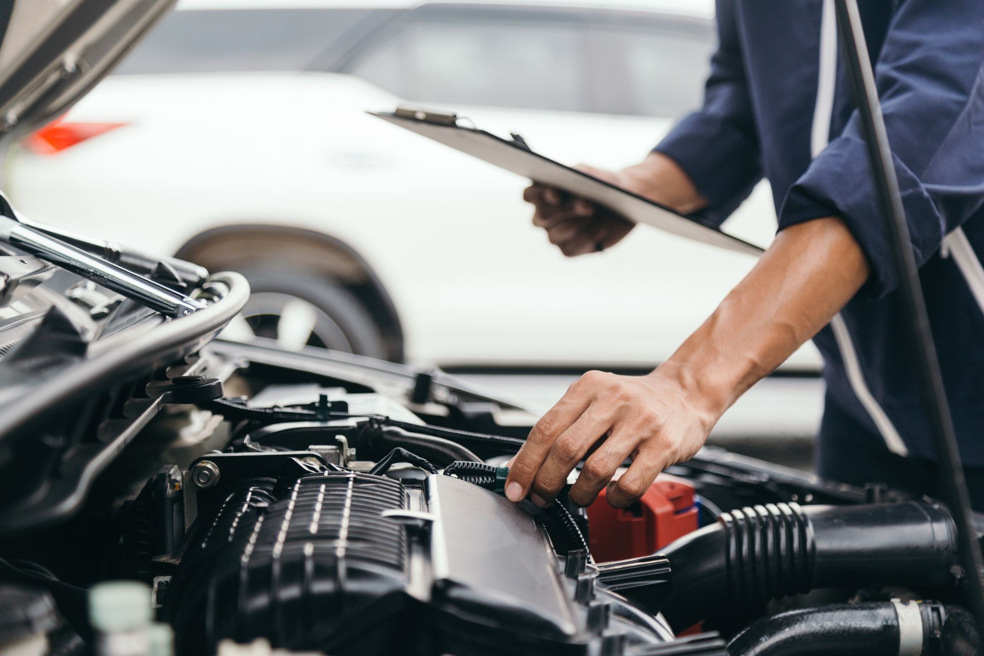 Mechanic inspecting car engine with clipboard. Outdoors, white car.