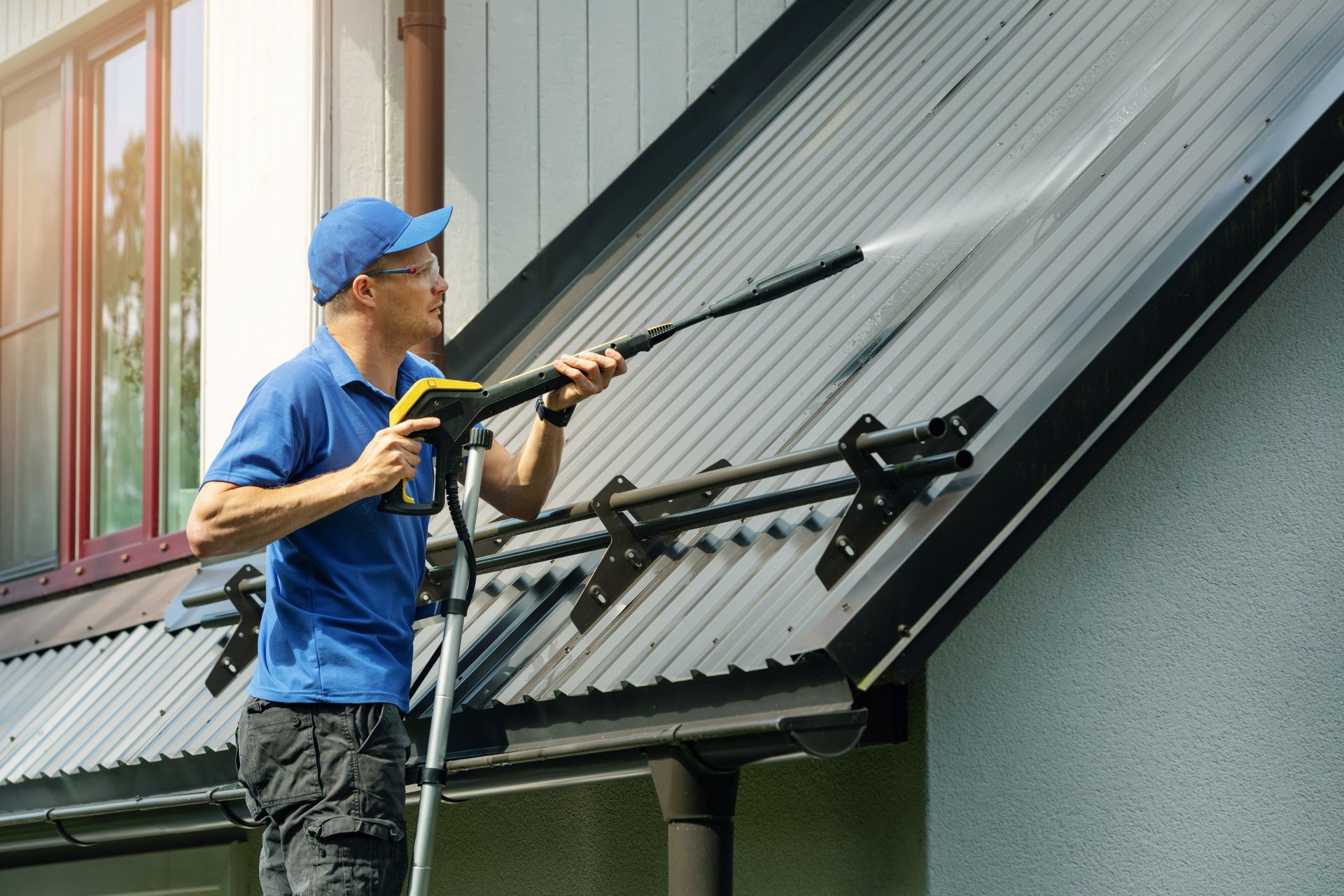 Person pressure washing a metal roof on a sunny day.