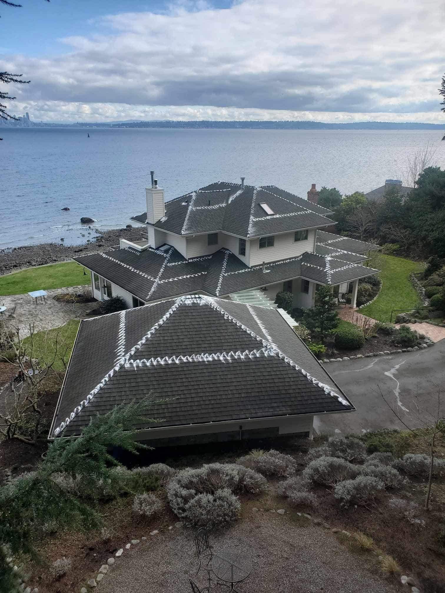 Large house with dark roof by the sea under a cloudy sky.