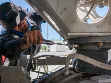 A person wearing a cap uses a wrench to tighten a bolt on a large industrial piece of machinery. | Kensington Motor Cars