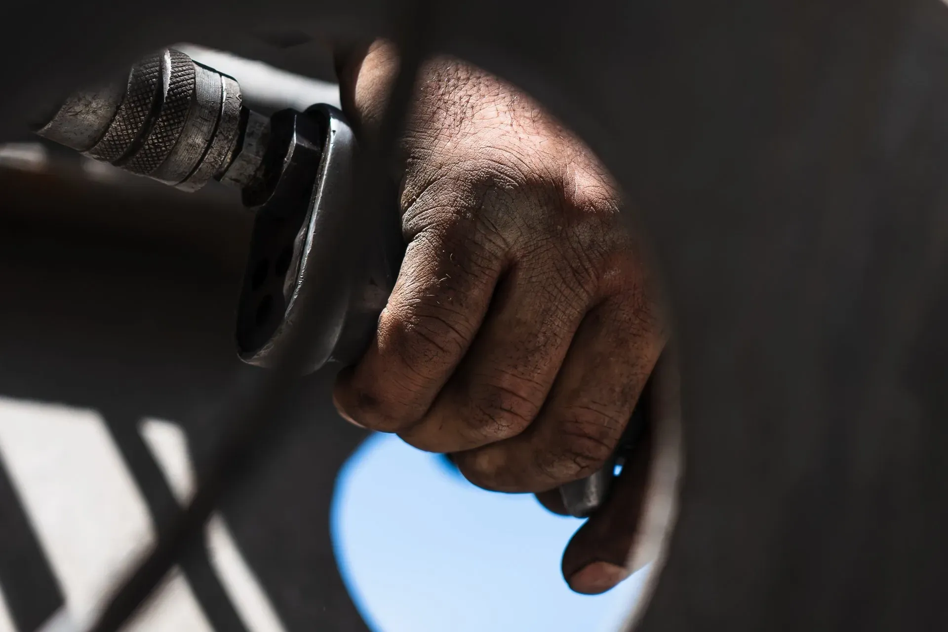 A close-up of a weathered, dirt-streaked hand gripping a dark mechanical tool against a blurred background. | Kensington Motor Cars
