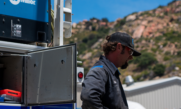 Man in workwear near open utility truck with mountainous backdrop. | California Coast Truck Repair