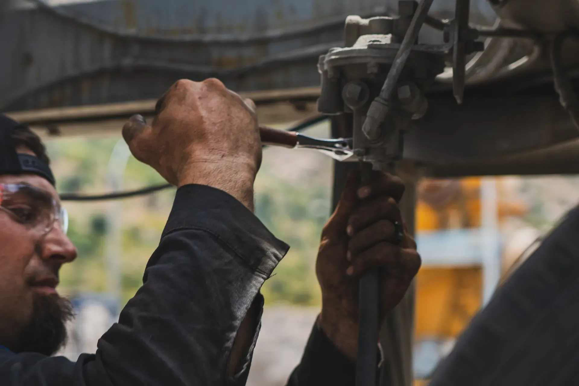 A mechanic wearing safety glasses uses a wrench to work on machinery. | Kensington Motor Cars