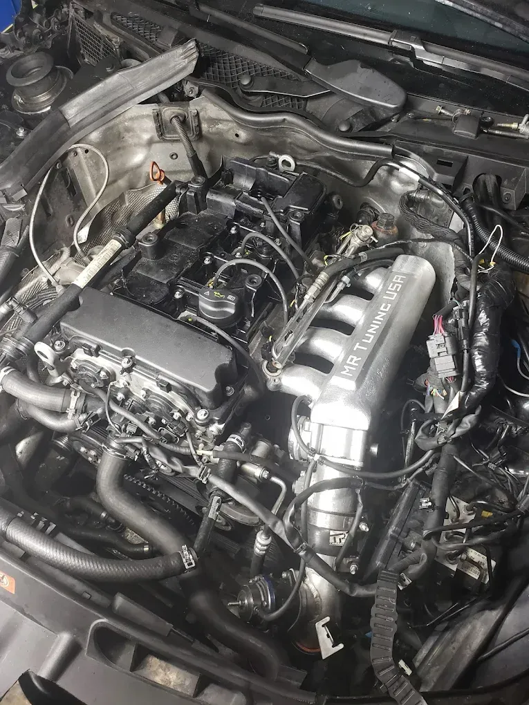 Engine bay of a car with exposed engine components, black and silver details, various hoses and wiring visible, in a repair setting.