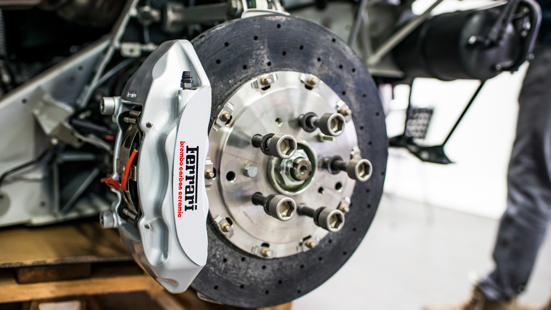 Ferrari car brake assembly with silver caliper and drilled disc rotor.