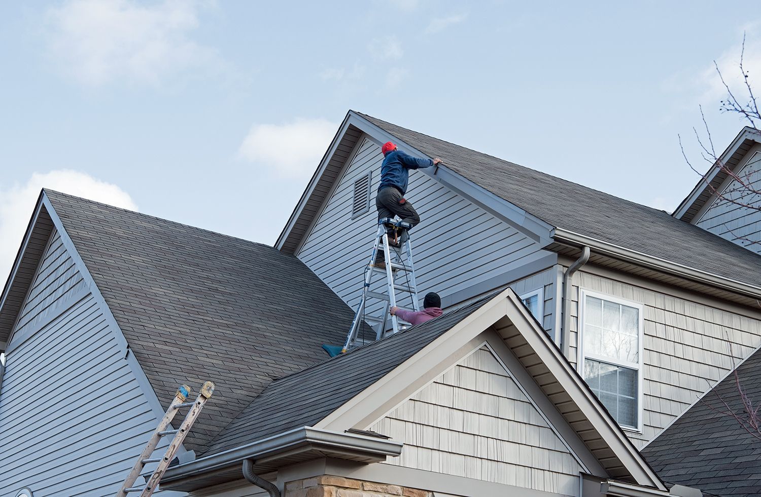 Worker on a steep roof using a ladder near a house chimney