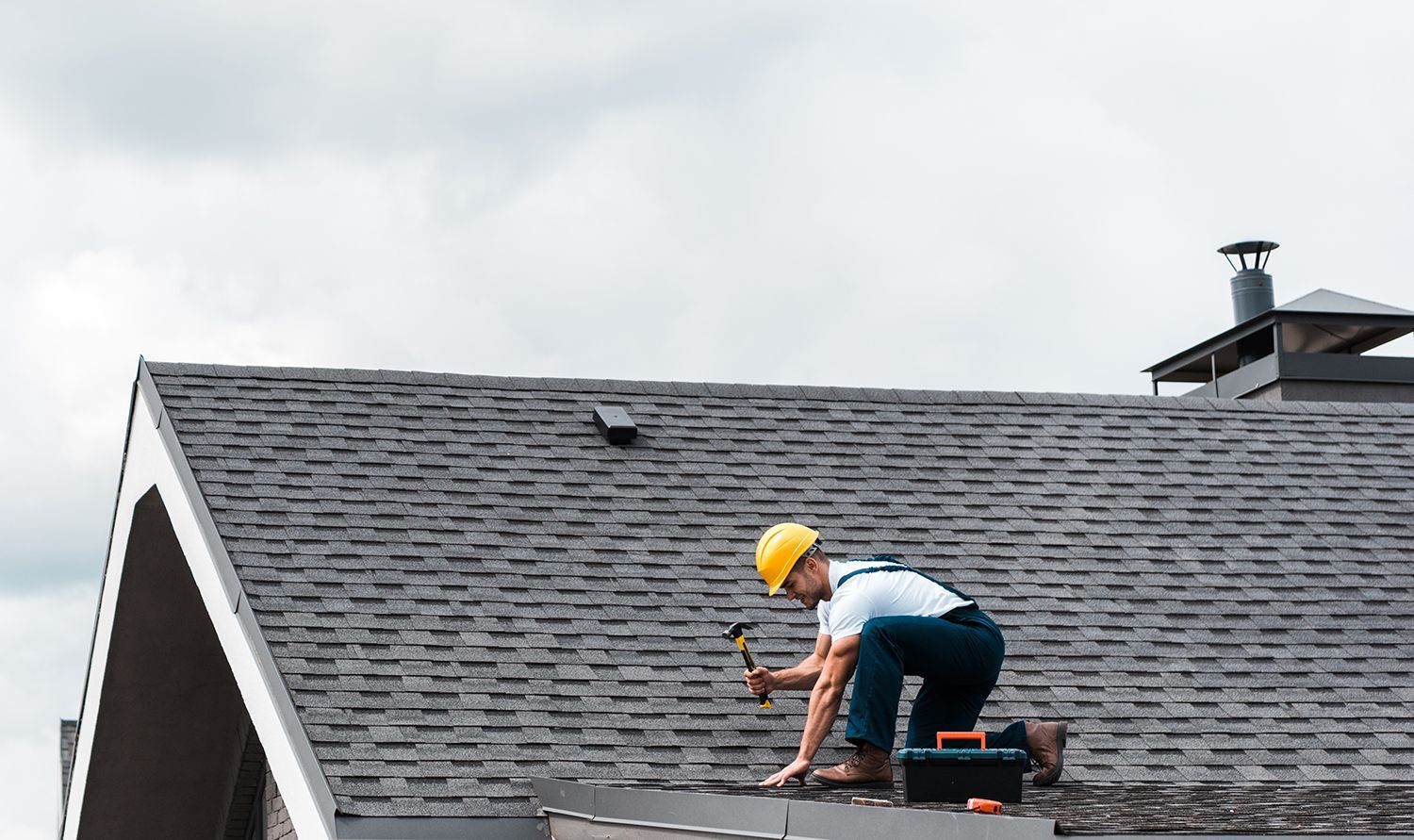 Worker on a roof installing shingles on a gray house rooftop Worker on a roof installing shingles on a gray house rooftop