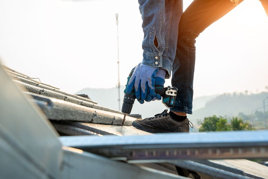 Worker using a nail gun on a rooftop under bright sunlight