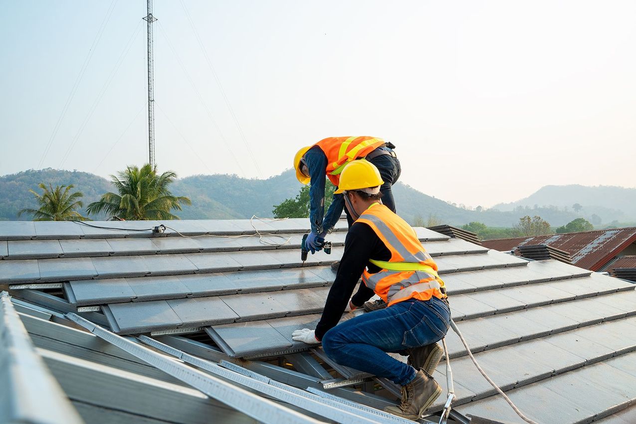 Two workers in yellow hard hats installing metal roofing on a rooftop outdoors