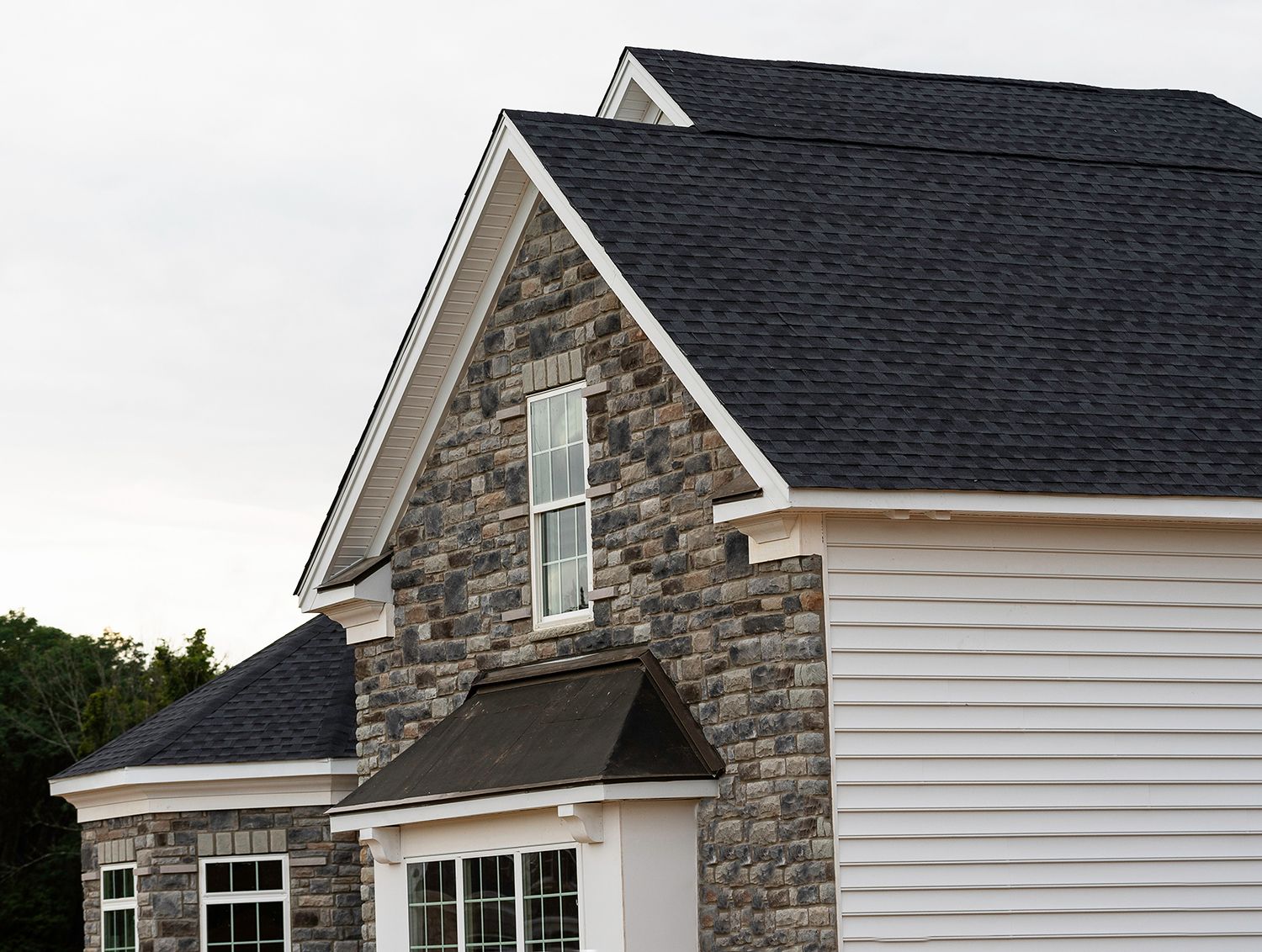 Stone-and-white house exterior with dark shingled roof and dormer windows