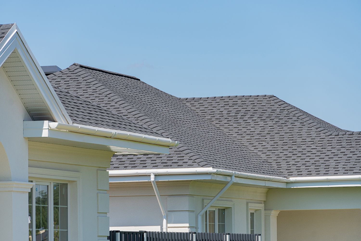 Suburban house roof with gray shingles and white trim under a clear blue sky