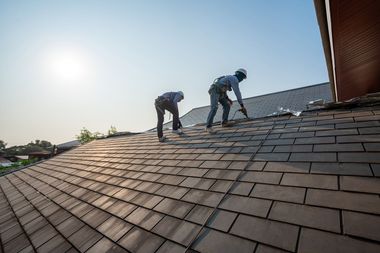Two workers installing roof tiles on a sloped roof in bright sunlight
