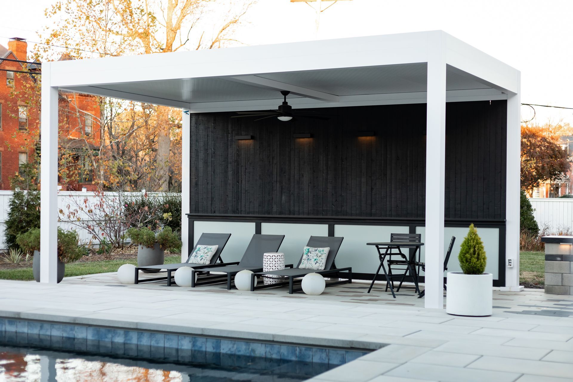 White pergola with a black accent wall, pool, lounge chairs, and a small table.