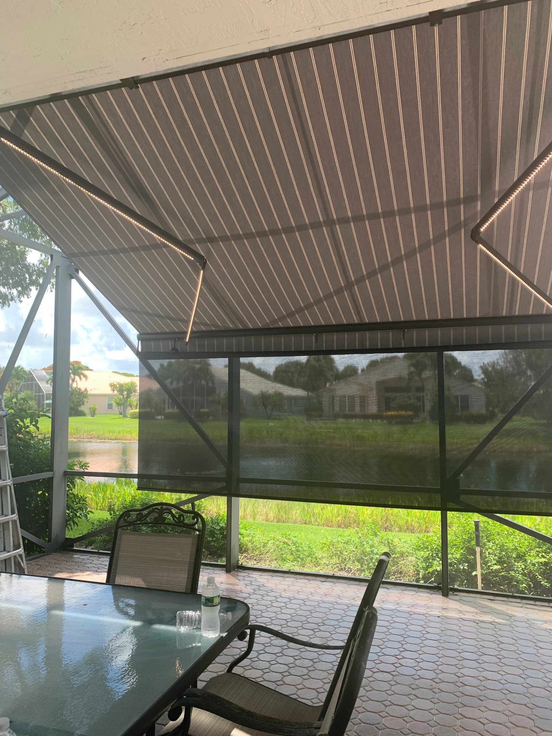 Patio with sun shades and screens overlooking a pond. Furniture visible.