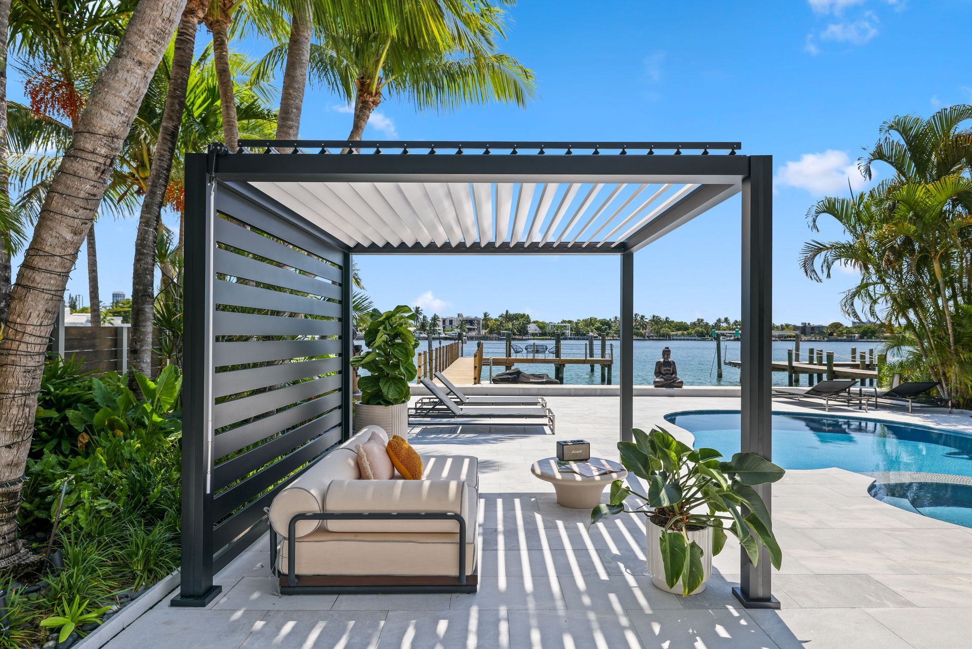 Modern outdoor patio with pergola, sofa, and pool overlooking water.