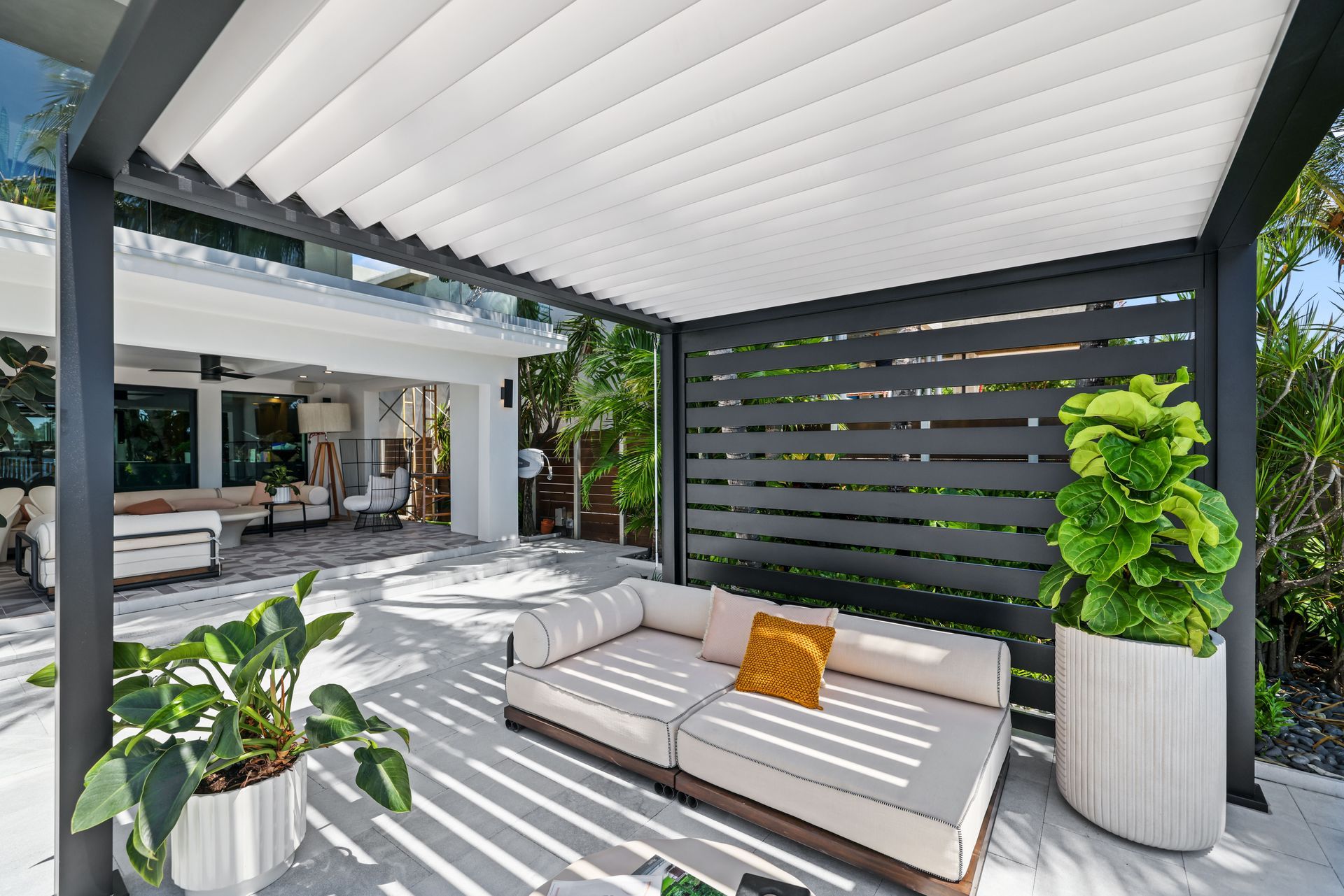 Outdoor patio with a white couch, green plants, and a gray pergola.