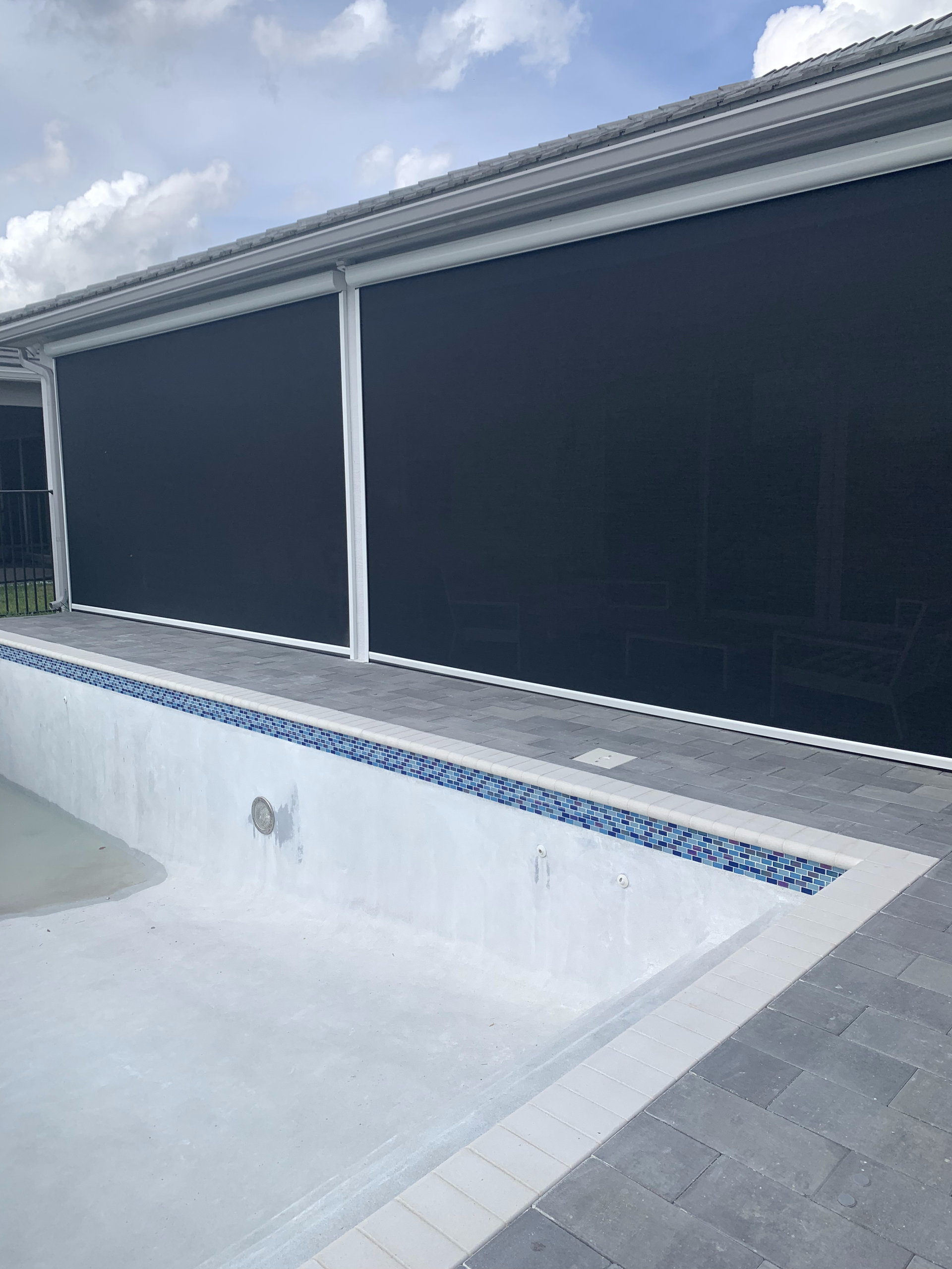 Pool with large black sun shades, white trim, and blue mosaic tile detail. Cloudy sky above.