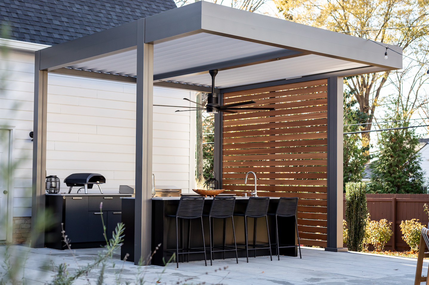 Outdoor kitchen with a pergola, bar seating, grill, and wood privacy screen.