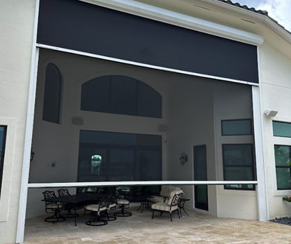 Large outdoor retractable black screen, protecting a patio with furniture. White house exterior.