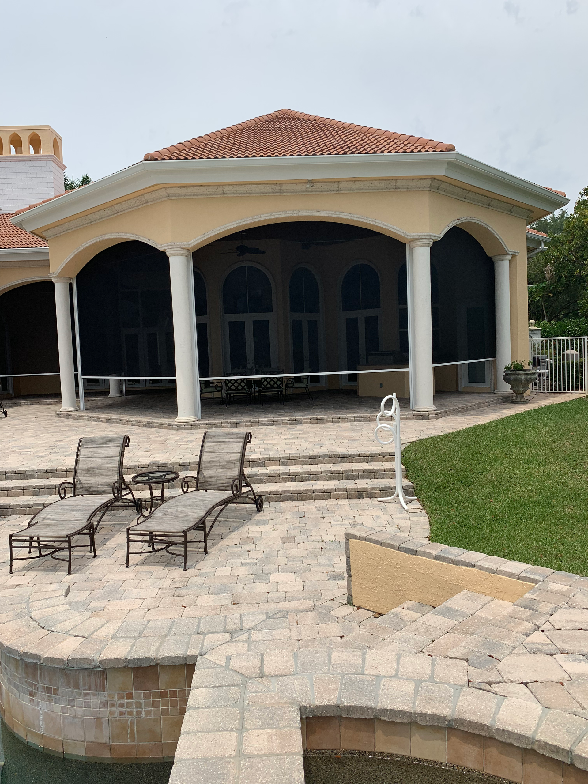 Poolside pavilion with beige exterior, white columns, and red tile roof. Lounge chairs sit on stone patio.