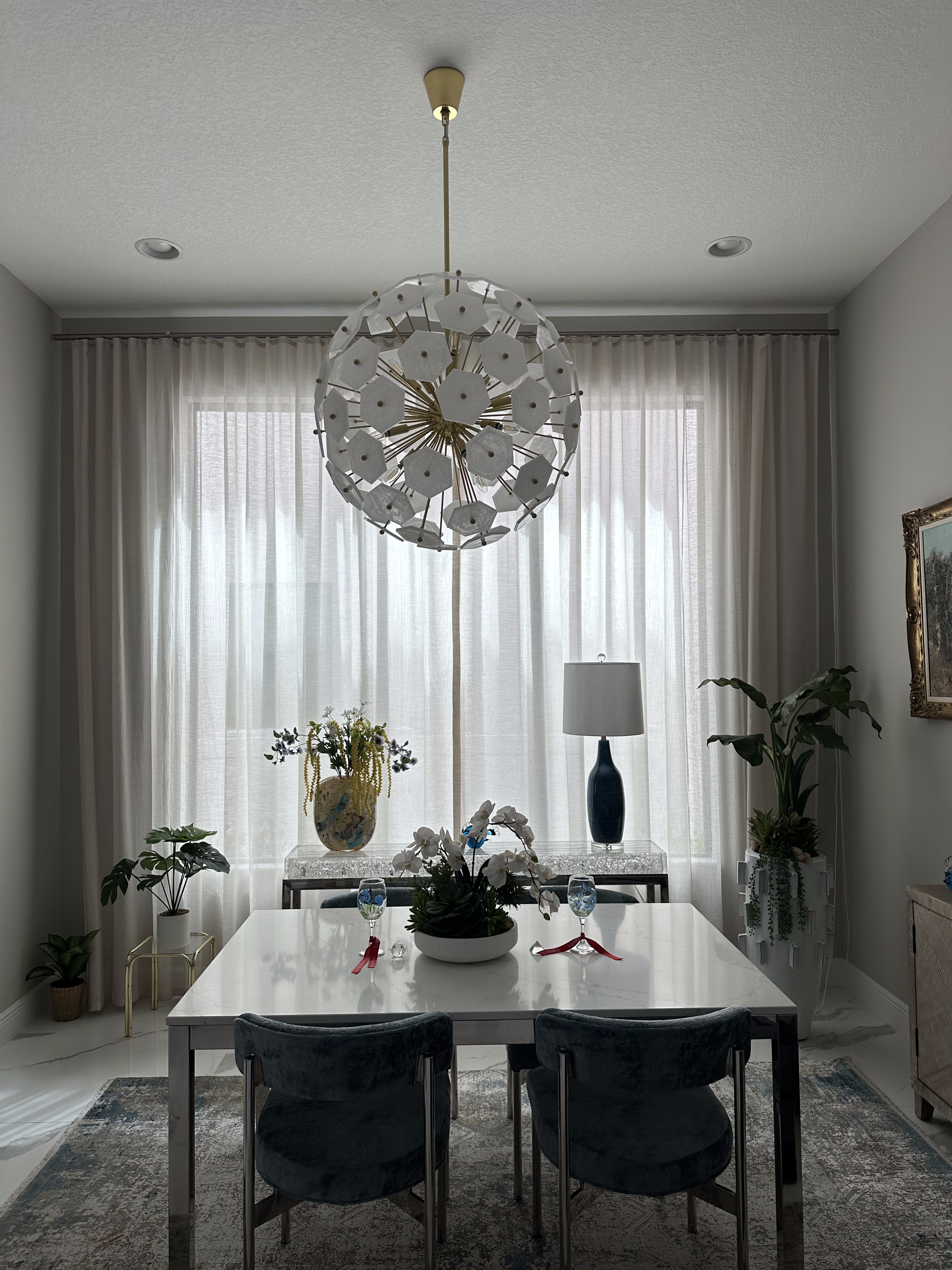 Dining room with a white table, chairs, curtains, and chandelier.