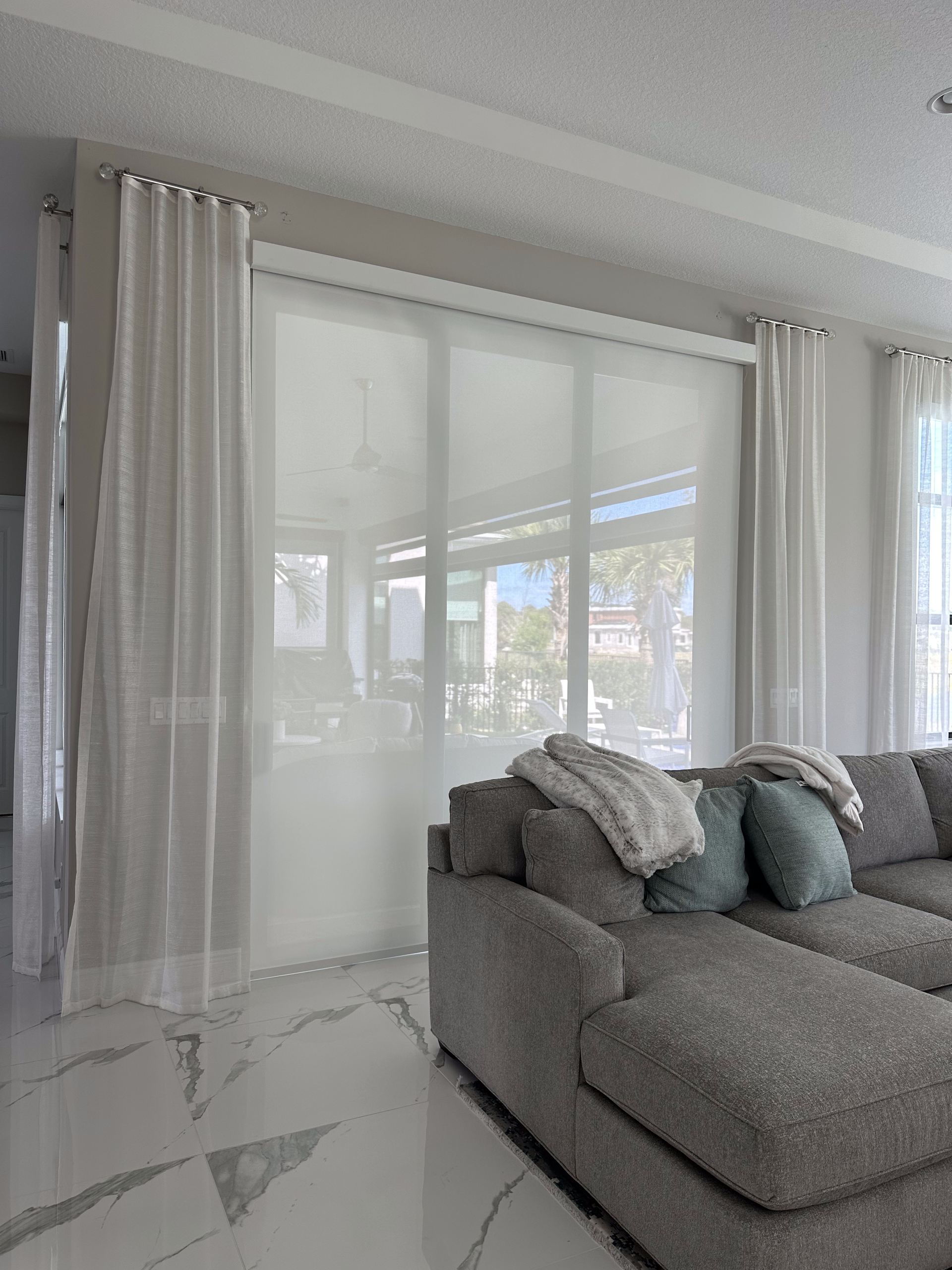 Living room with sheer white curtains, light gray couch, and large windows.