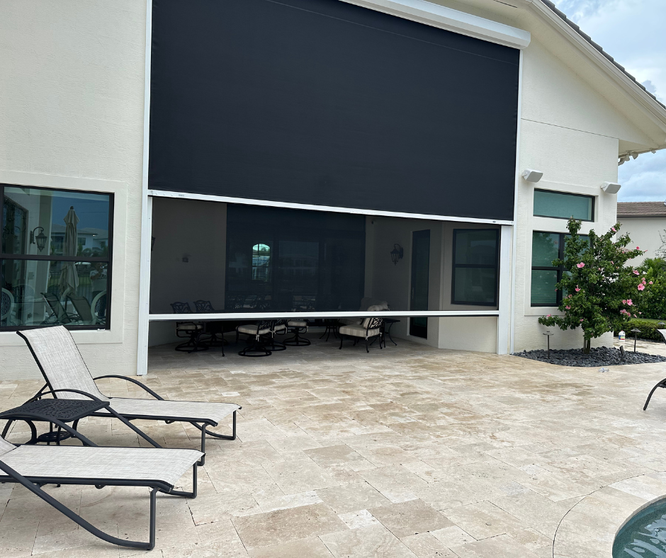 Black retractable screen on a patio, partially lowered, shading an outdoor seating area.