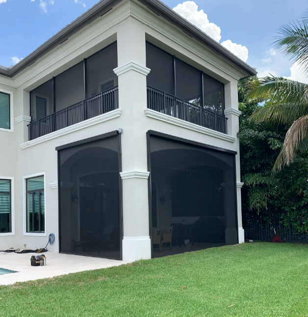Two-story white house with black screens on the porch and balcony; green lawn.