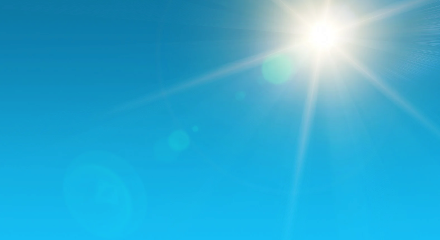 Bright sun shining in a clear blue sky. Lens flares and light rays radiate from the sun.