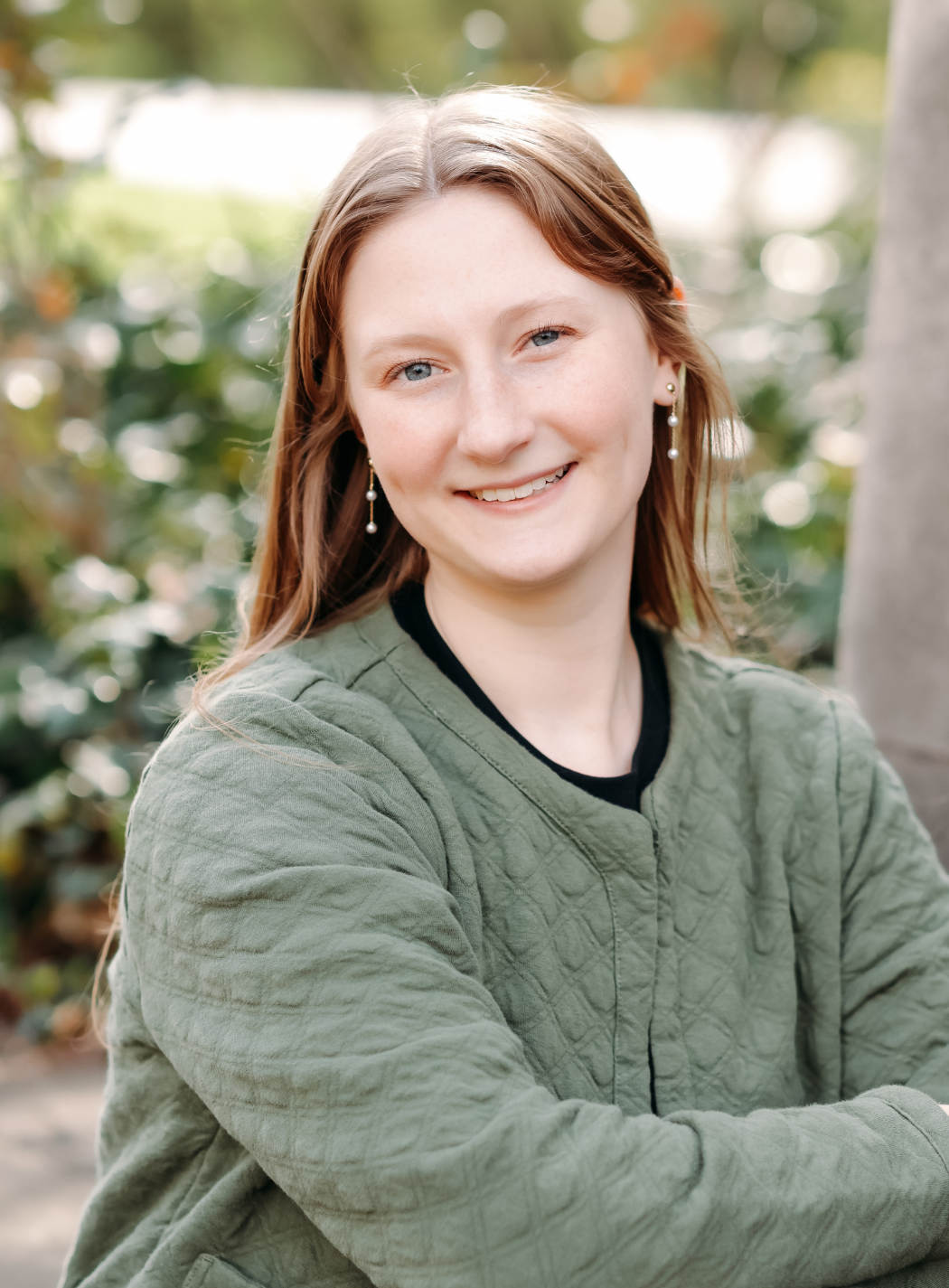 Woman in black and white striped cardigan, sitting, smiling, on a dark gray backdrop.