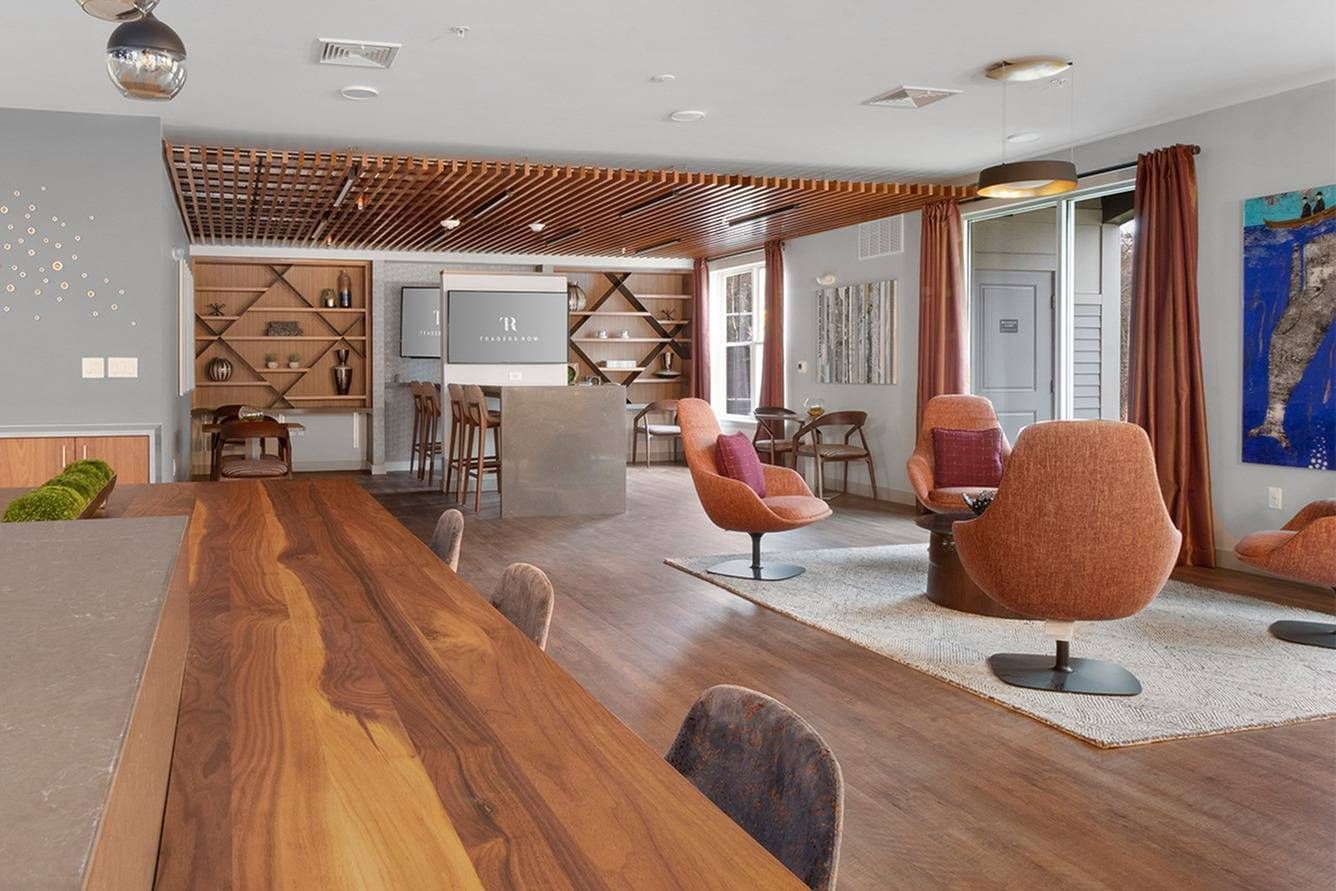 Modern open-plan living room with wood ceiling, pink chairs, and a long wooden dining table