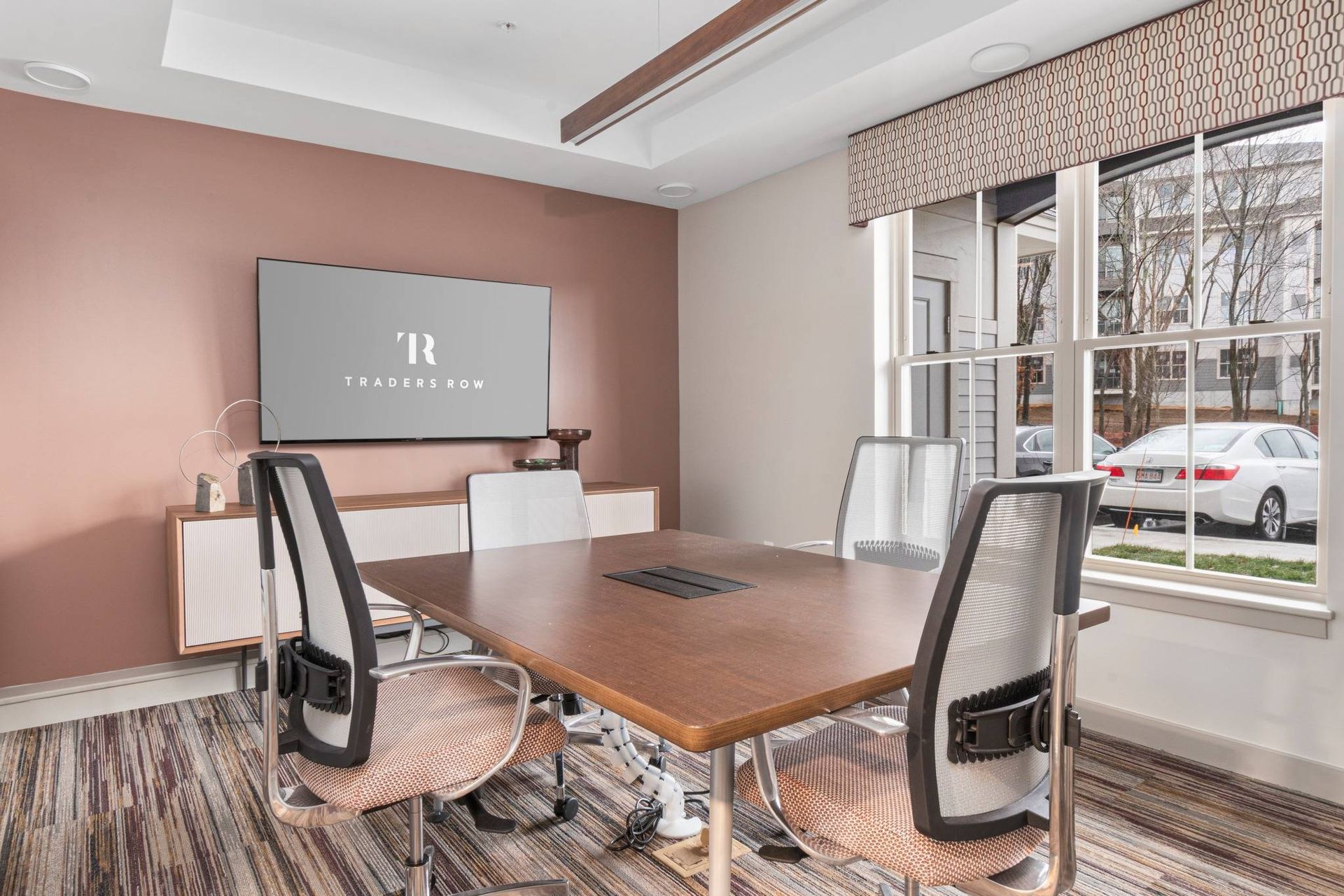 Modern conference room with wooden table, white chairs, wall screen, and large window.