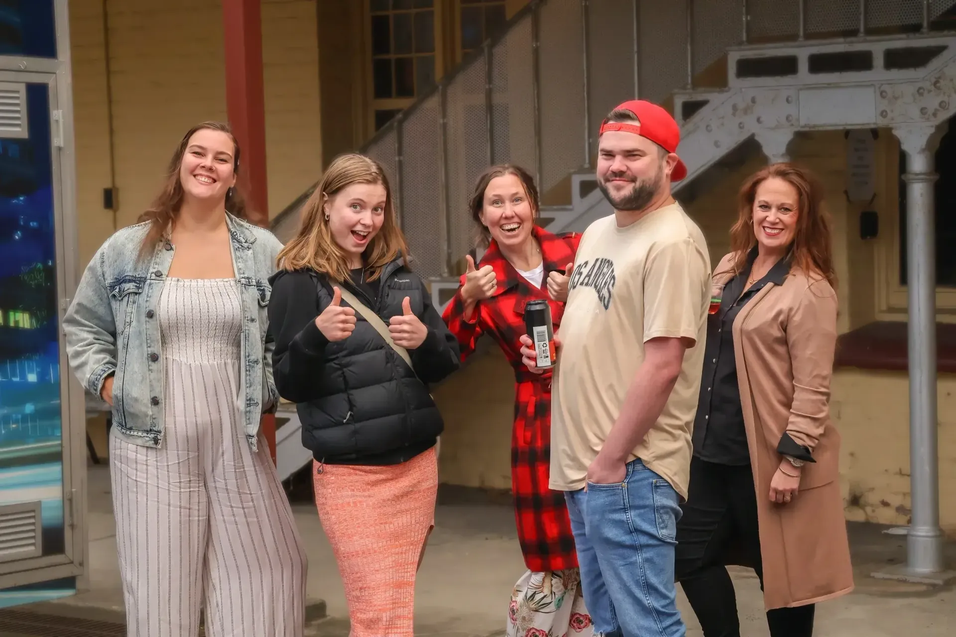 Five people smiling outdoors, dressed in casual and festive clothes, standing in front of a porch.